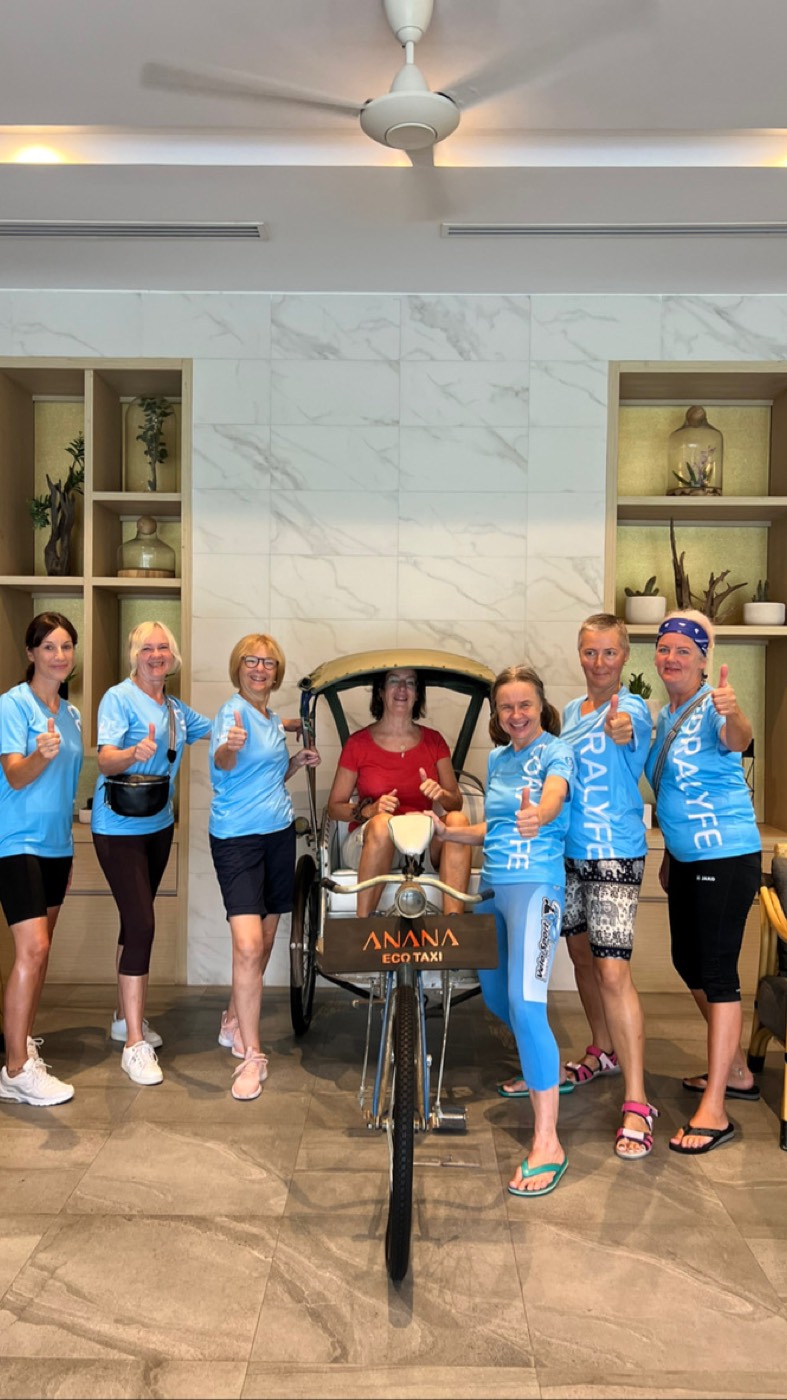 Frauen in blauen Shirts mit Daumen hoch um eine Rikscha
